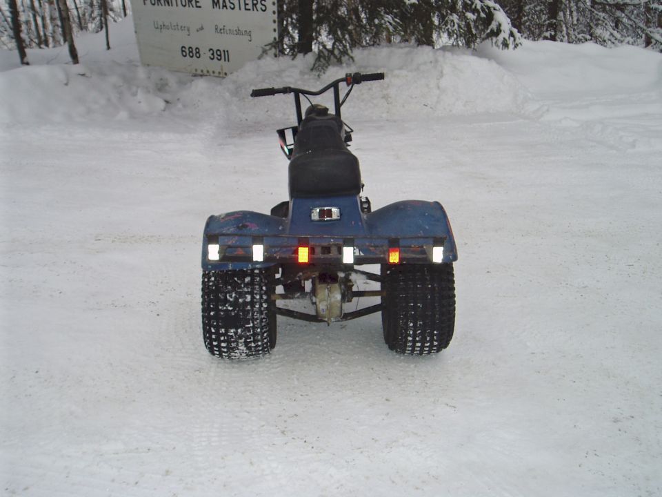 Rear view of blue three-wheeler ATC with reflectors on snow, sign and snowbanks behind