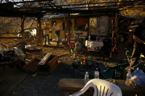 1986 Ford Bronco - A casual outdoor scene unfolds with people gathered near a rustic cabin, a campfire providing warmth and ambiance.