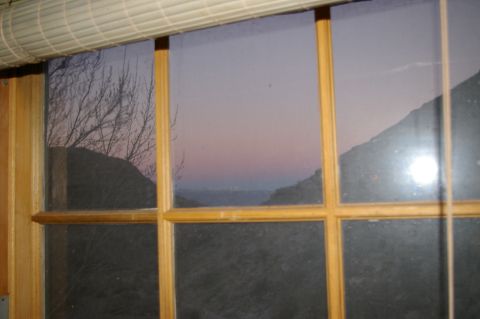 1986 Ford Bronco - A tranquil landscape unfolds through a window at twilight, with bare branches and rolling hills under a soft sky.