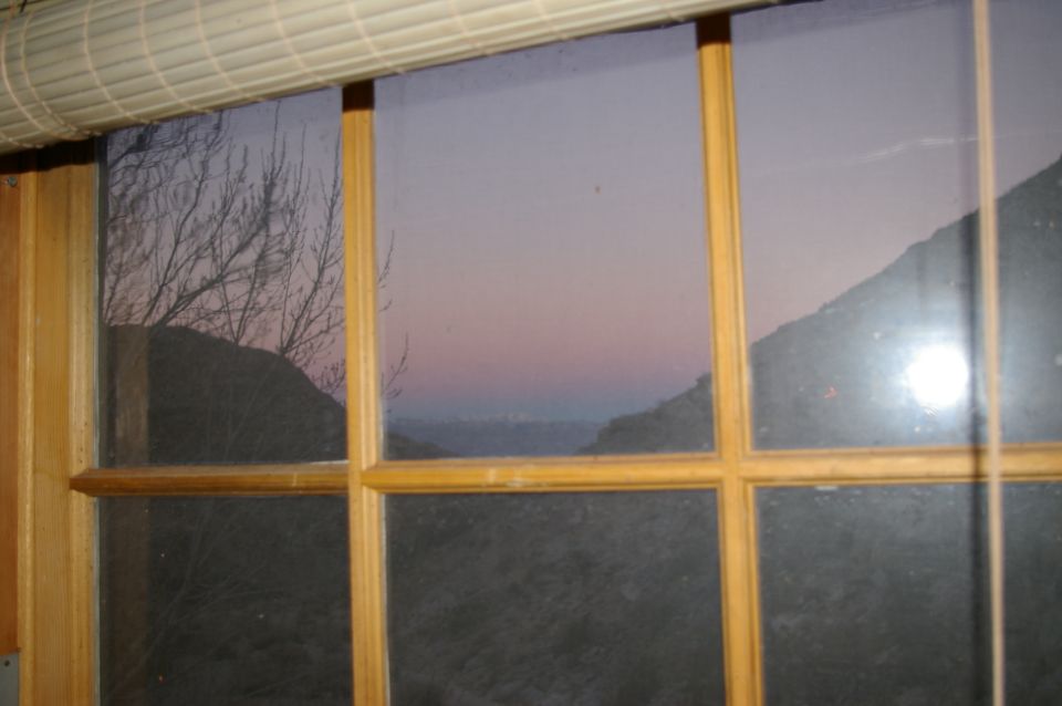 View through a window with wooden frames at dusk, showing silhouetted trees and hills