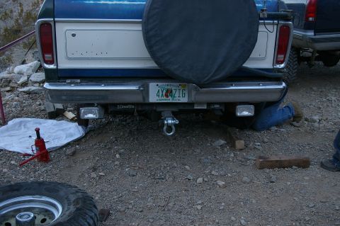 1986 Ford Bronco - A person works on the rear of a blue and white Ford truck, with another truck visible to the right.