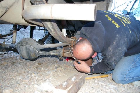 1986 Ford Bronco - A person is crouched down, examining the rear axle and suspension components of a vehicle.
