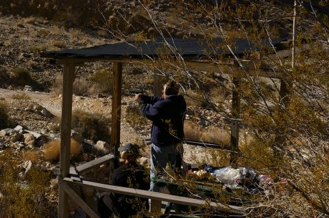1986 Ford Bronco - Two individuals practice shooting at an outdoor range with a wooden shelter and arid landscape.
