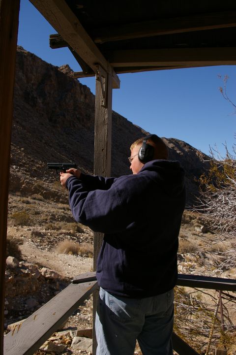 1986 Ford Bronco - A person wearing ear protection aims a handgun at an outdoor shooting range with a mountainous backdrop.