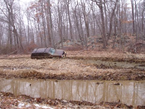 1976 Toyota Land Cruiser - An off-road vehicle is partially submerged in a muddy track surrounded by trees.