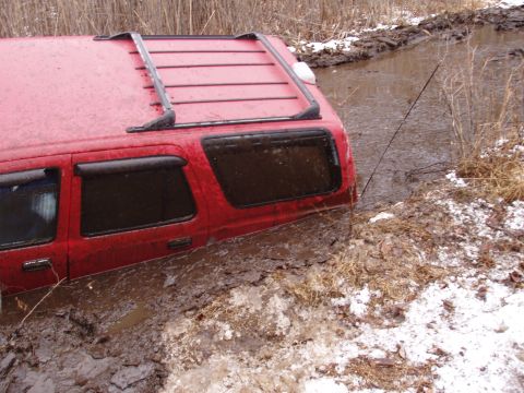 1976 Toyota Land Cruiser - A red SUV is stuck in a muddy ditch with dry grass and some snow on the banks.