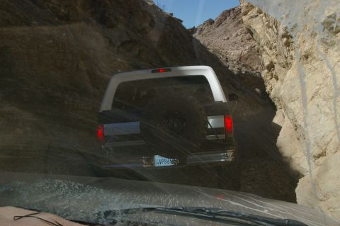 1986 Ford Bronco - This 1986 Ford Bronco navigates a tight passage in a rocky canyon, its rear taillights and spare tire visible.