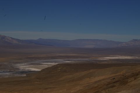 1986 Ford Bronco - A wide, arid landscape stretches towards distant mountains under a bright blue sky, with patches of dry lakebed visible in the mid-ground.