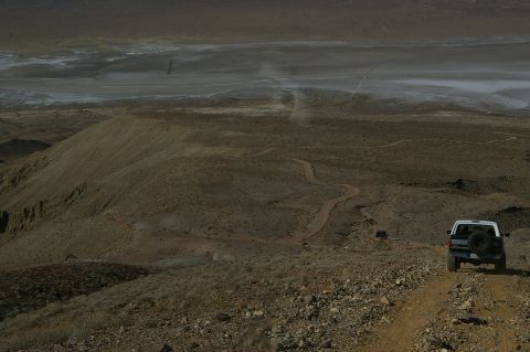 1986 Ford Bronco - A white 1986 Ford Bronco navigates a dusty trail through a barren, arid landscape.
