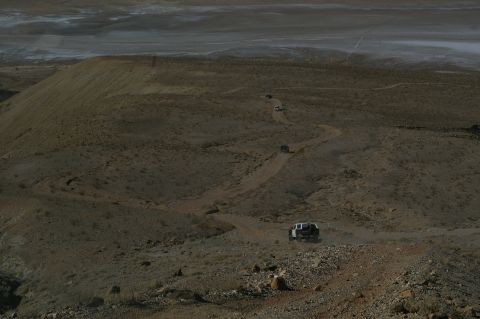 1986 Ford Bronco - A convoy of vehicles navigates a dusty, winding path through a barren, hilly terrain.
