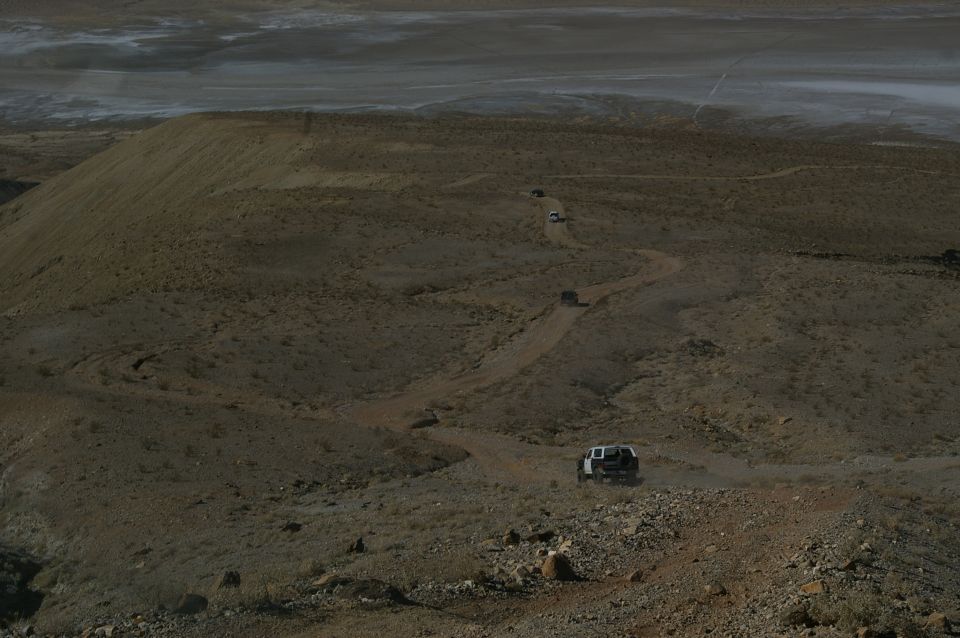 Several SUVs driving up a winding dirt road in a desert landscape