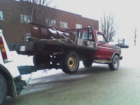 1992 Ford Bronco - A red flatbed truck, likely from the 1970s, is being towed while carrying a snow plow.