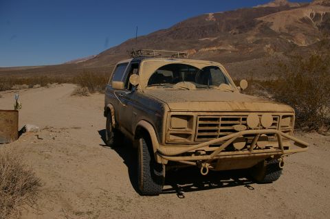 1986 Ford Bronco - A dusty Ford Bronco sits in a dry, arid environment with mountains in the background.