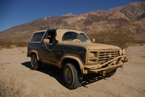 1986 Ford Bronco - A dusty 1986 Ford Bronco sits in a desert landscape with mountains in the background.