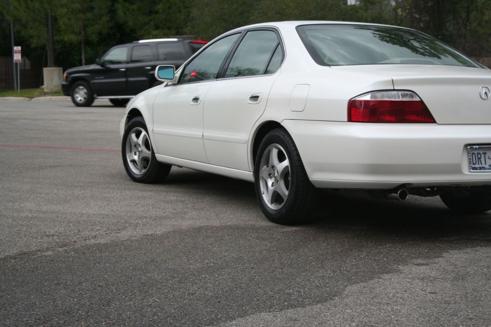Low rear 3/4 close-up of a white Acura TL sedan's tail lamp and alloy wheels