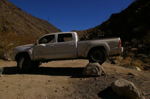 1986 Ford Bronco - A white pickup truck navigates a rocky, off-road trail under a clear blue sky.