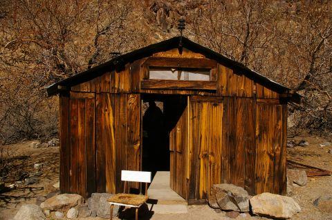 1986 Ford Bronco - A rustic wooden cabin stands open to the elements, with a simple chair placed near the entrance.