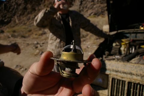 1986 Ford Bronco - Close-up of a car thermostat part being held, with a person and vehicle in the background.