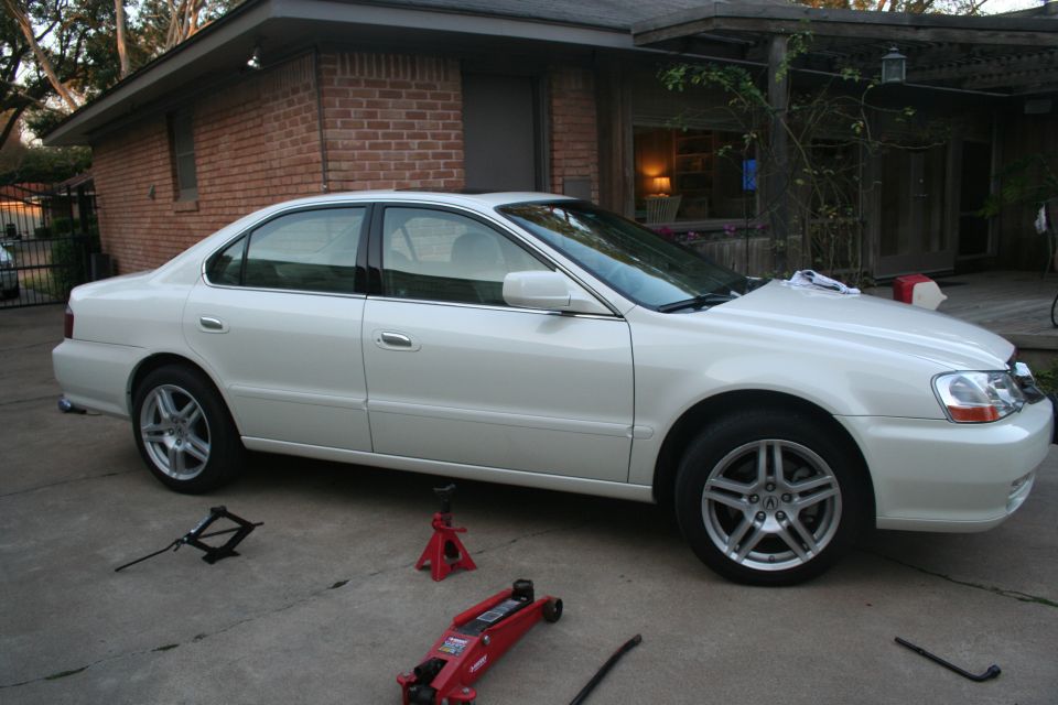 White Acura TL sedan on driveway with floor jack, jack stands and lug wrench laid out