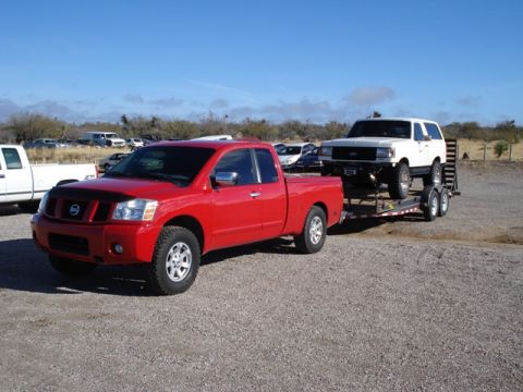 2005 Nissan Titan - A red 2005 Nissan Titan pickup truck tows a trailer carrying a white SUV on a sunny day.