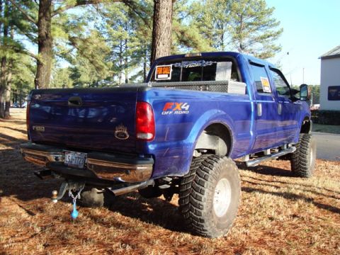2003 Ford F-250 - A lifted blue Ford F-250 pickup truck is parked outdoors with a "For Sale" sign visible in the rear window.