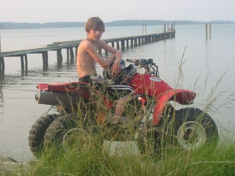 1978 Ford F-250 - A boy sits on a red ATV by the water with a pier in the background.