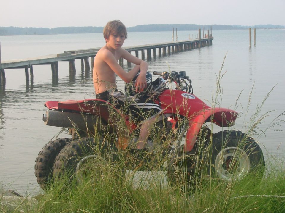 Boy sitting on red ATV near a wooden pier and a lake