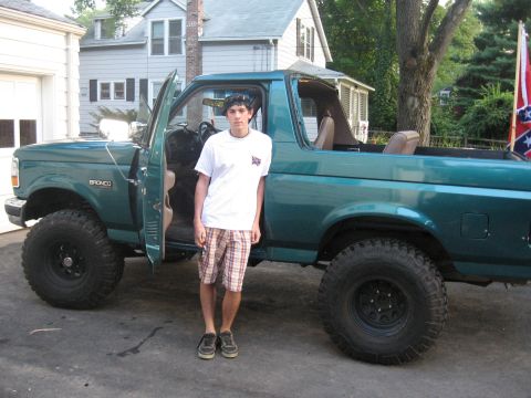 1996 Ford Bronco - Side view of a lifted teal-green Ford Bronco with the hardtop removed, driver's door open showing a tan interior and the BRONCO fender badg…