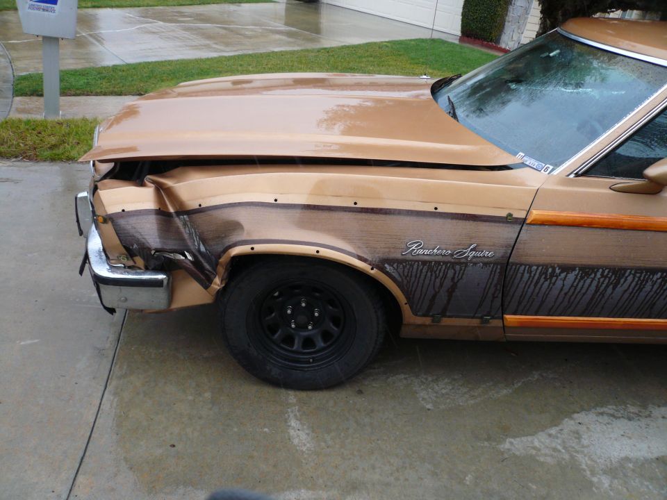 Front fender and bumper are crumpled on a brown Ford Ranchero Squire with wood paneling. The vehicle is parked on a wet driveway