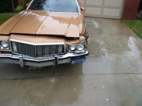 1975 Ford Ranchero - A damaged 1975 Ford Ranchero sits in front of a garage on a wet day.