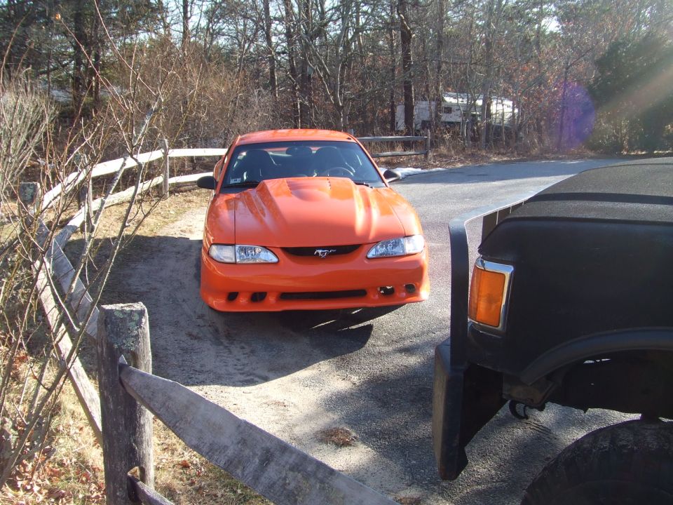 Orange Ford Mustang with a hood scoop parked next to a black truck
