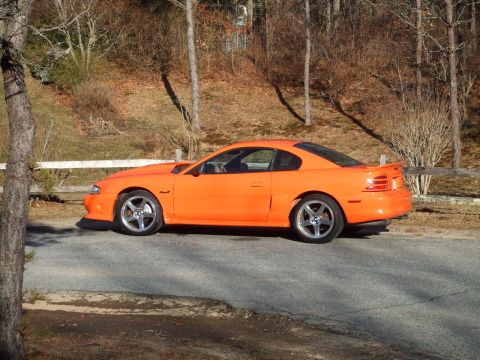 1995 Ford Mustang - Side view of an orange 1995 Ford Mustang coupe parked outdoors.