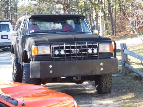 1995 Ford Mustang - This black SUV features a prominent custom bumper and large off-road tires, partially obscuring an orange vehicle in the foreground.