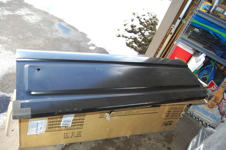 Dark gray automotive body panel on a CERTIFIED cardboard box in a snowy garage area.