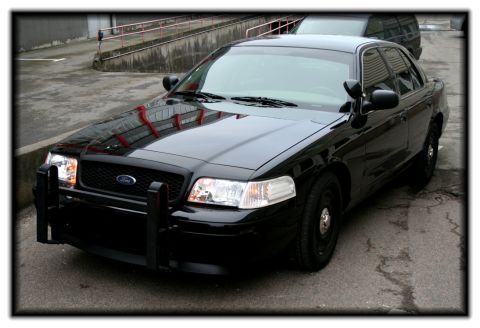 1998 Ford Crown Victoria - A black police car is parked outside next to another vehicle.