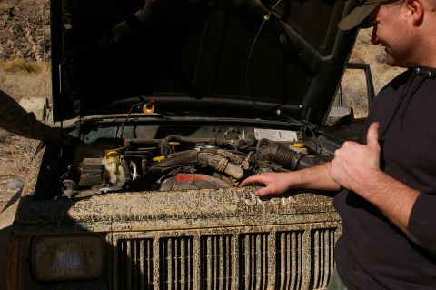 1986 Ford Bronco - Two men inspect the engine bay of a muddy Jeep with its hood open.