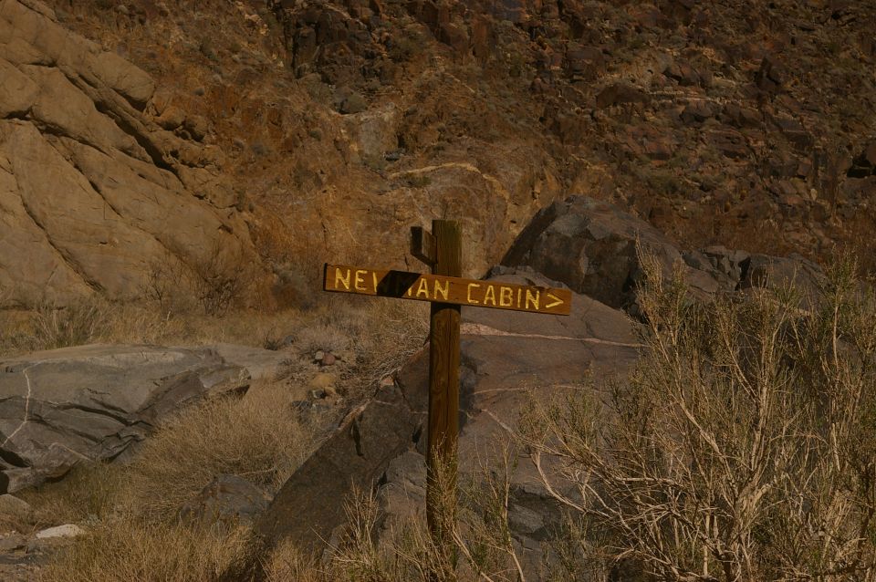 Wooden signpost with "NEYMAN CABIN" text pointing right, set against rocky desert landscape