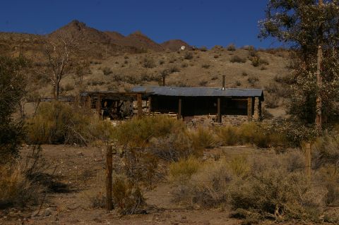 1986 Ford Bronco - An old stone building with a corrugated metal roof sits in a dry, brush-filled landscape under a clear blue sky.