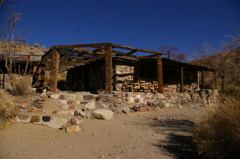 1986 Ford Bronco - Rustic stone building with a wooden pergola and chairs in a dry, outdoor setting.