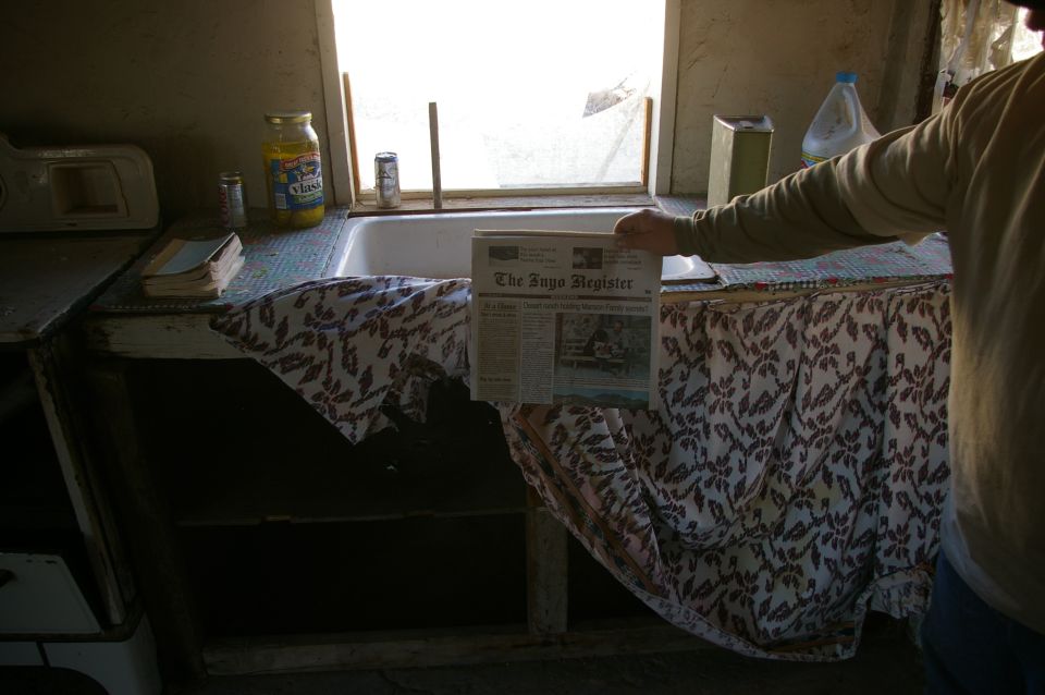Newspaper titled 'The Toyo Register' held over a kitchen counter with a sink and jar of pickles