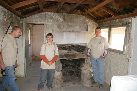 1986 Ford Bronco - The interior of a rustic structure features a stone fireplace and exposed wooden ceiling beams, with three individuals present.