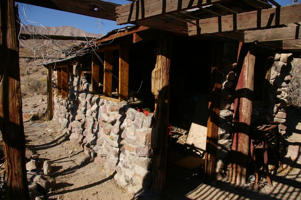 Abandoned stone building with wooden roof supports and dry brush in a desert landscape