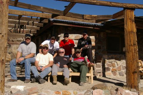 1986 Ford Bronco - Men relax in front of a stone structure under a clear blue sky.