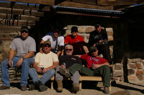 1986 Ford Bronco - Seven men are gathered outdoors, seated on a bench in front of a rustic stone structure.