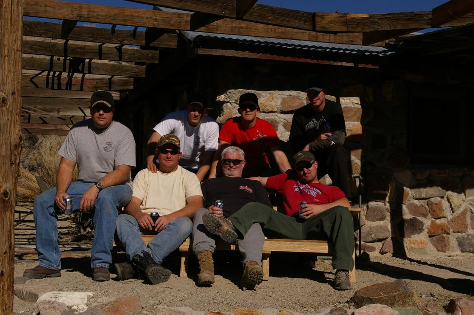 Group of men sitting on a bench outside a rustic stone building
