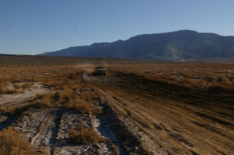 1986 Ford Bronco - Vehicle navigates a dusty trail in a vast, arid landscape under a clear blue sky.