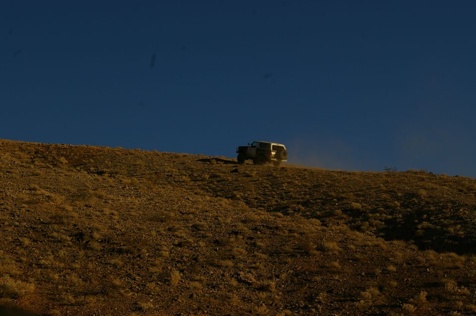 1986 Ford Bronco driving up a dry, grassy hill with a clear blue sky