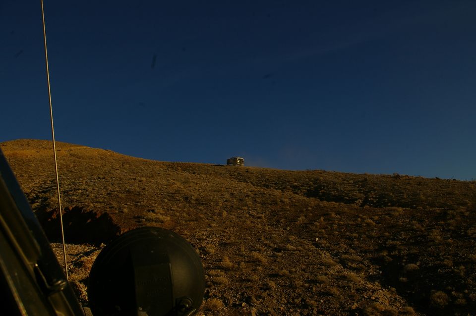 View from inside a vehicle looking out at a distant SUV on a grassy hill under a clear blue sky