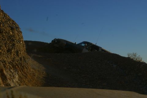 1986 Ford Bronco - An off-road vehicle navigates a steep, rocky incline against a bright blue sky.