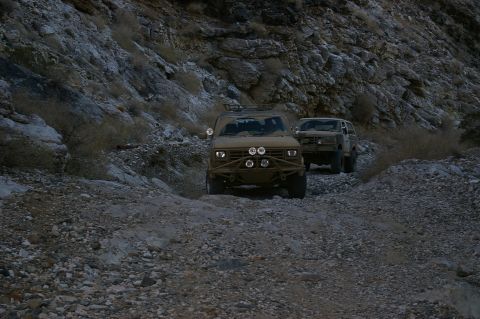 1986 Ford Bronco - Two SUVs navigate a challenging rocky path in a desert canyon environment.